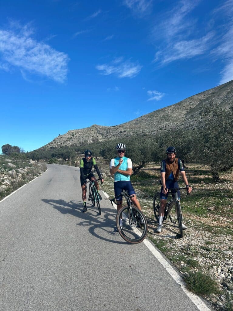 Tres ciclistas de Ezz Baily en una carretera de montaña entre olivos durante el training camp de Altea
